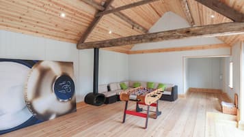 A wooden-floored room with a high ceiling, a sofa with green cushions, and a foosball table.