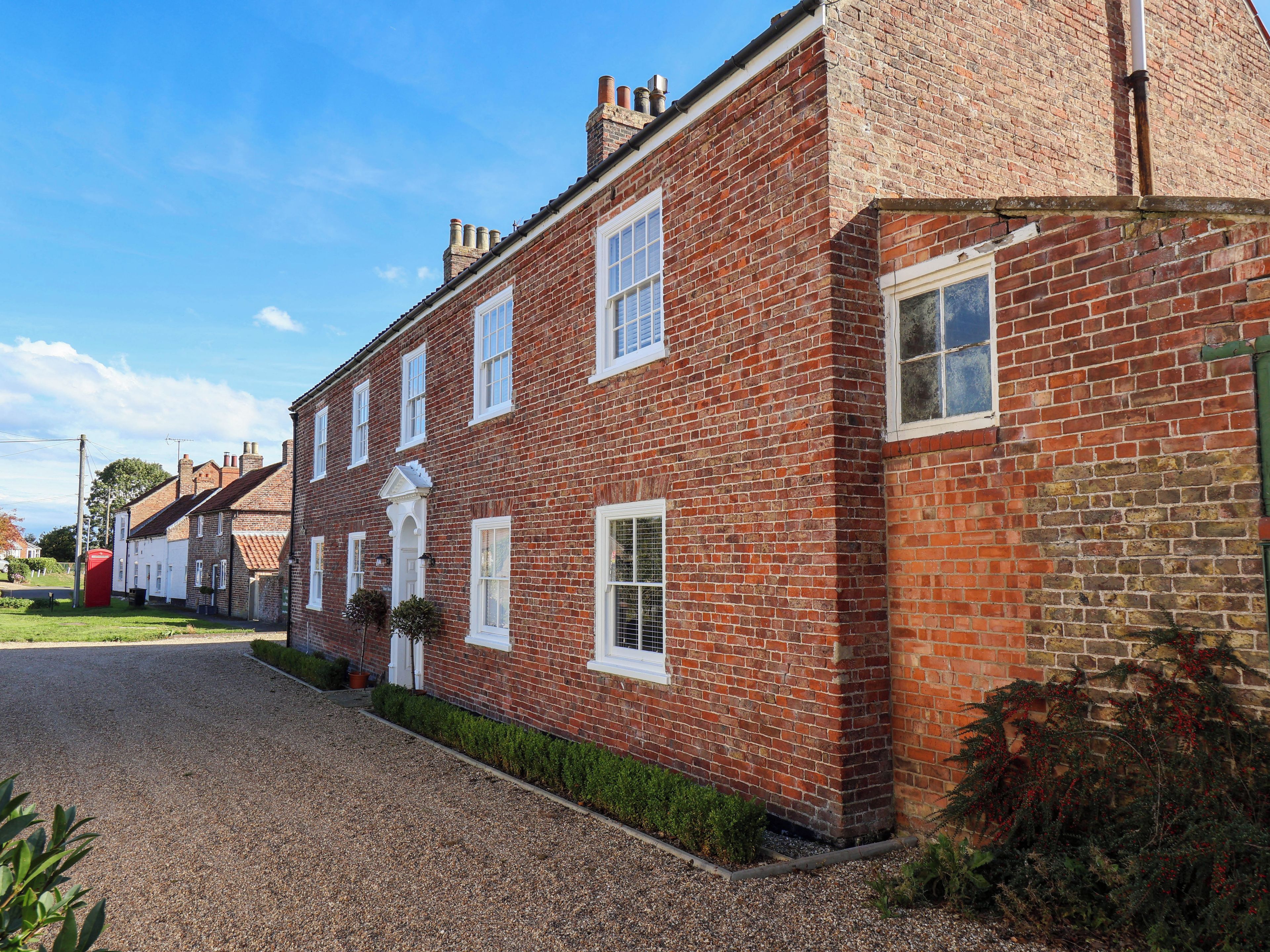 A traditional brick house with a gravel driveway and a red telephone box in the background.