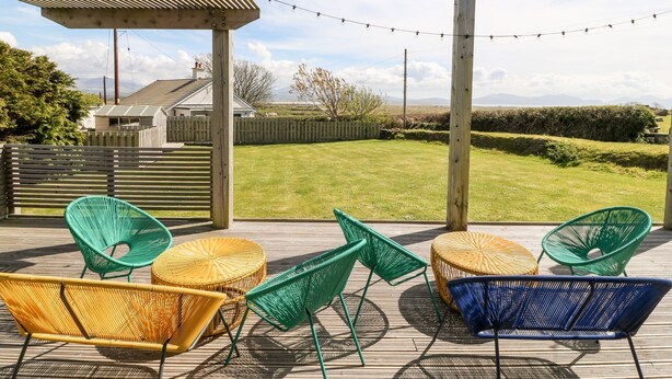 Eine Terrasse im Freien mit Korbmöbeln, einer Holz-Pergola und Blick auf ein Grasfeld sowie entfernte Berge.