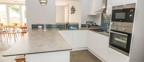 Een moderne keuken met witte kasten, een groot eiland, een inbouwoven en een hanglamp.