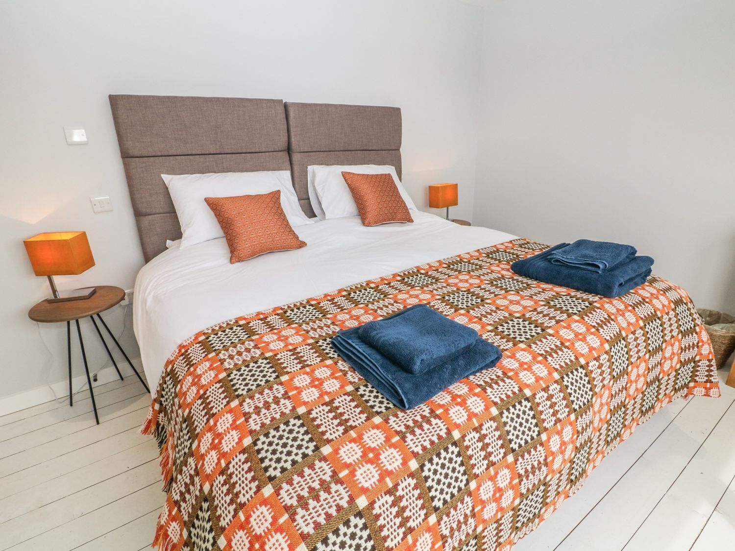 Een net opgemaakt bed met een bedsprei met patroon, twee kussens en opgevouwen handdoeken op een witte matras.