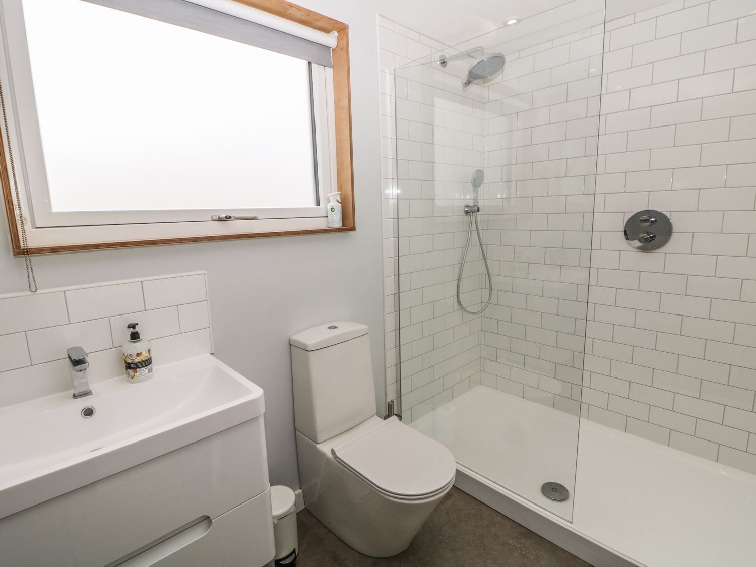 Et moderne badeværelse med bruseniche i glas, toilet og et håndvaskspejl.