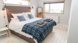Ein modernes Schlafzimmer mit einem großen Bett, einem Nachttisch, einem Spiegel und einem Fenster mit Blick.