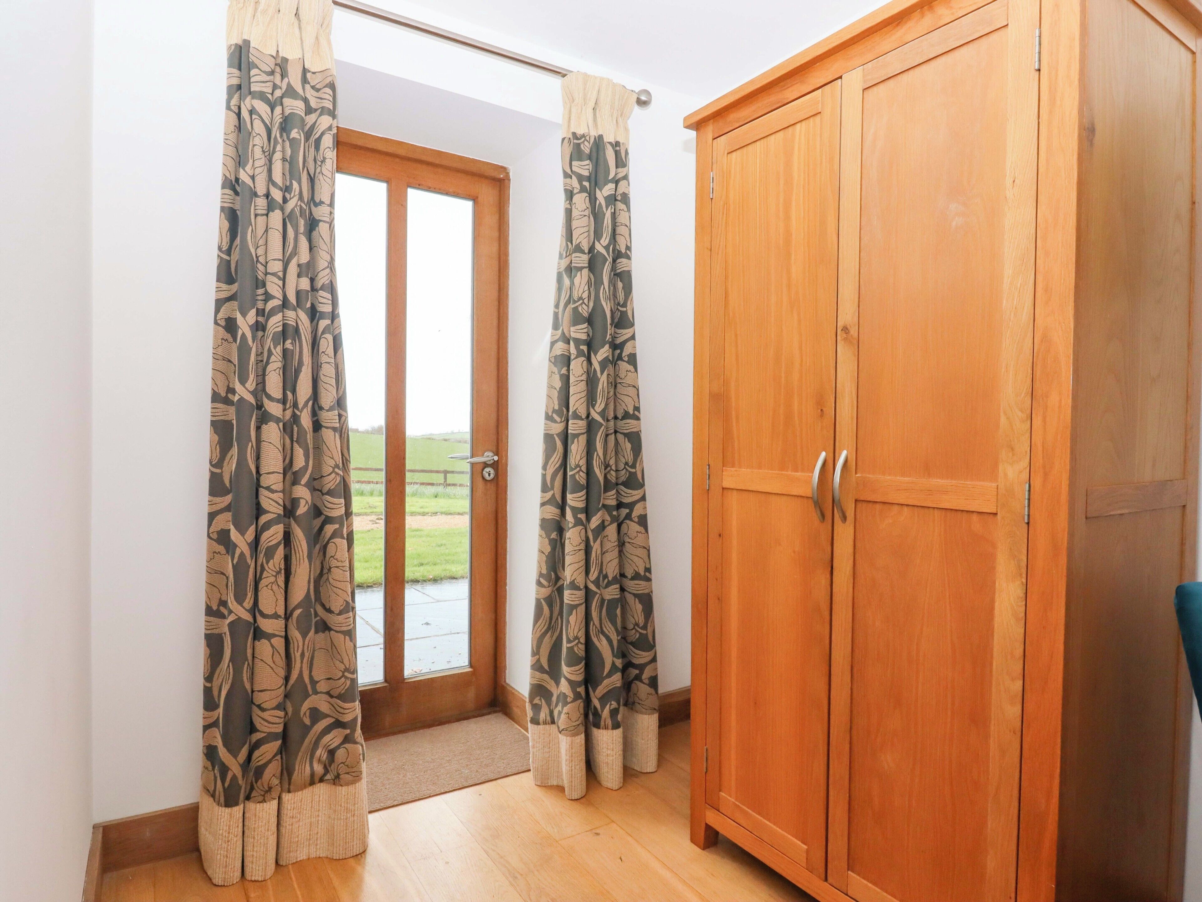 Una habitación con un armario de madera, una puerta con paneles de vidrio y cortinas estampadas.