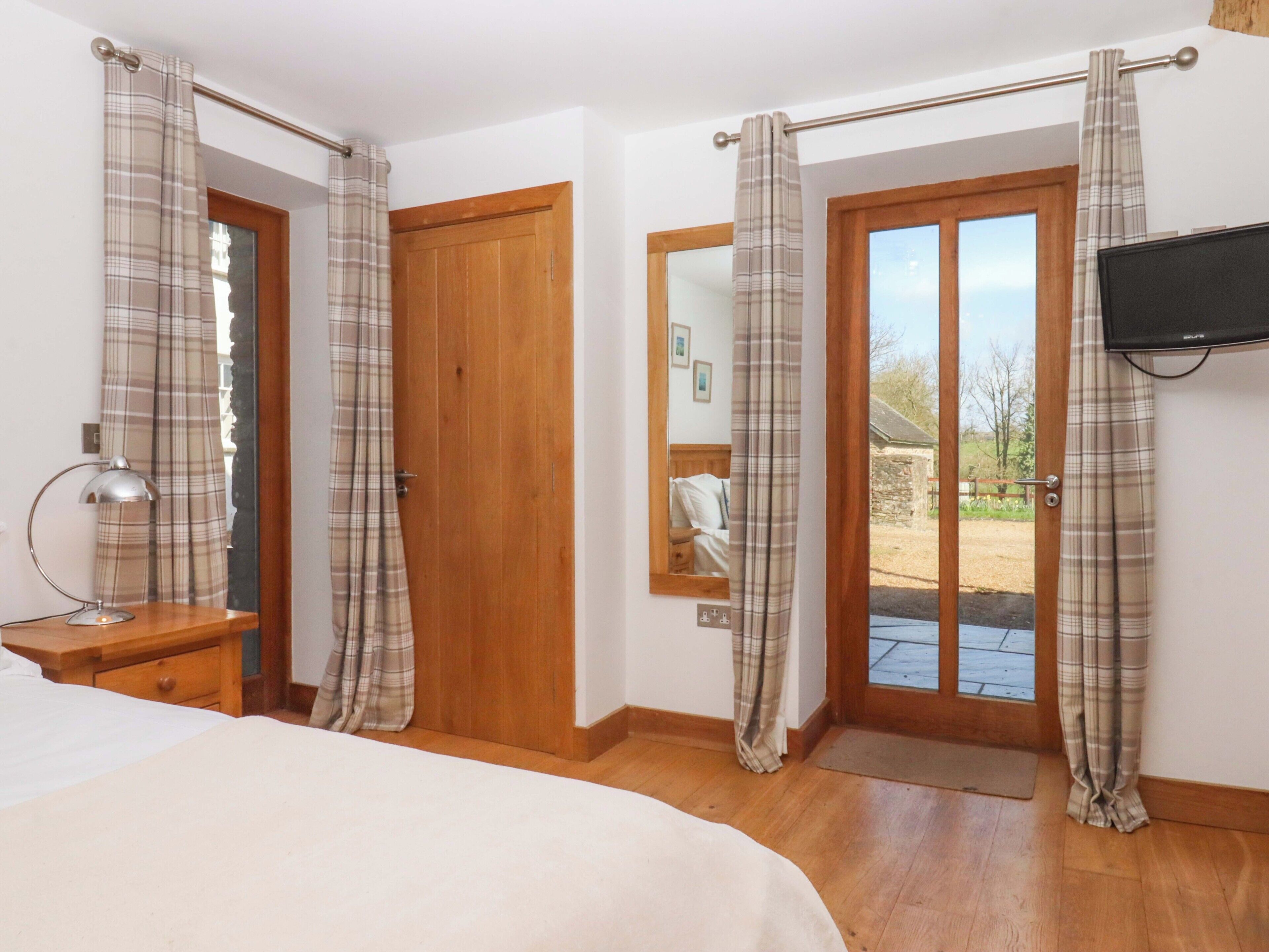 A bedroom with a bed, a wooden door, a mirror, a television, and a view of the outdoors.