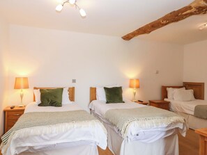 Quarto de hotel com duas camas, cada uma com mesa de cabeceira e luminária, viga de madeira no teto e design simples e limpo.