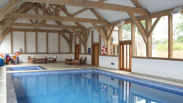 An indoor swimming pool with wooden beams, a lifebuoy, and a bench area. - Swallows Reach (Totnes)