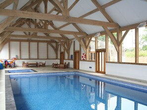 Piscina interior com vigas de madeira, um salva-vidas e área com bancos.