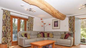A living room with a grey sofa, a wooden coffee table, a red patterned rug, and a large wooden beam ceiling. - Swallows Reach (Totnes)