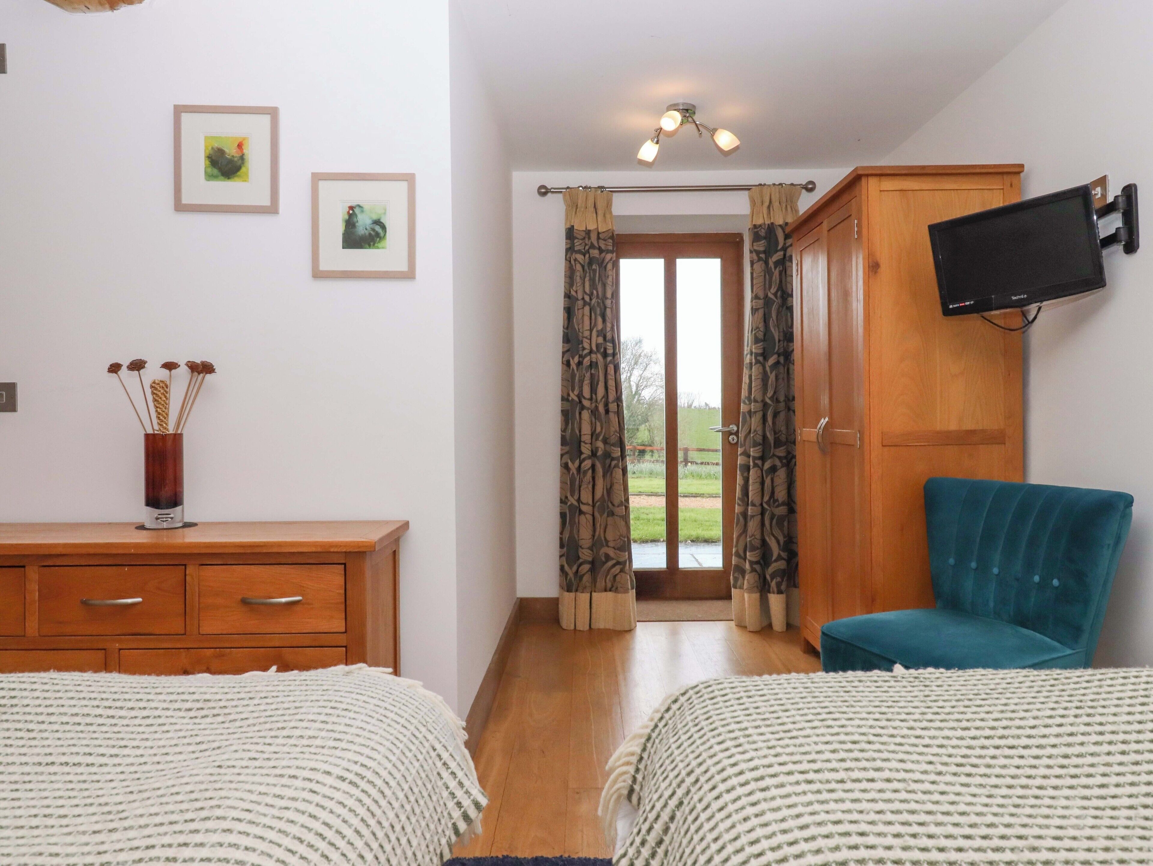 Une chambre avec deux lits, une armoire en bois, un téléviseur fixé au mur et une vue à travers les rideaux.