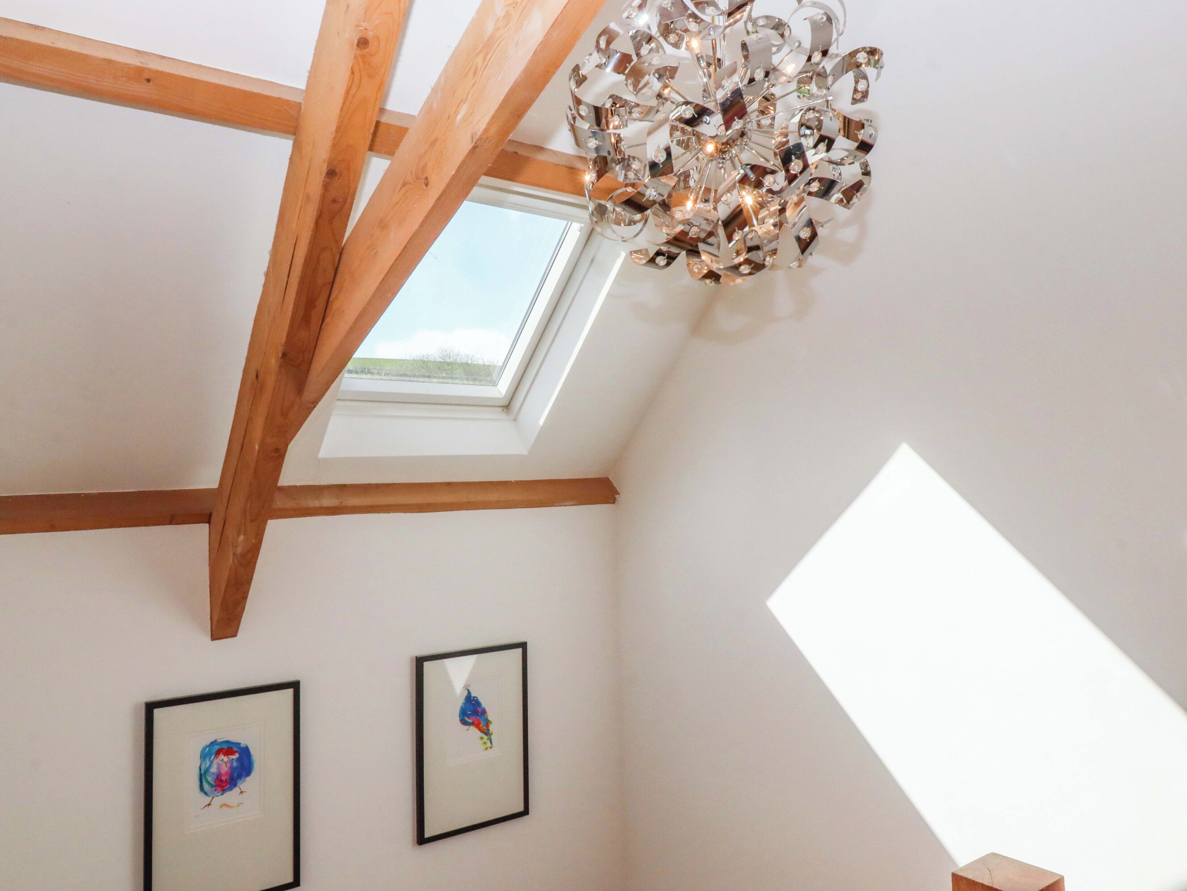 A room with wooden beams, a skylight, and two framed artworks on the wall.