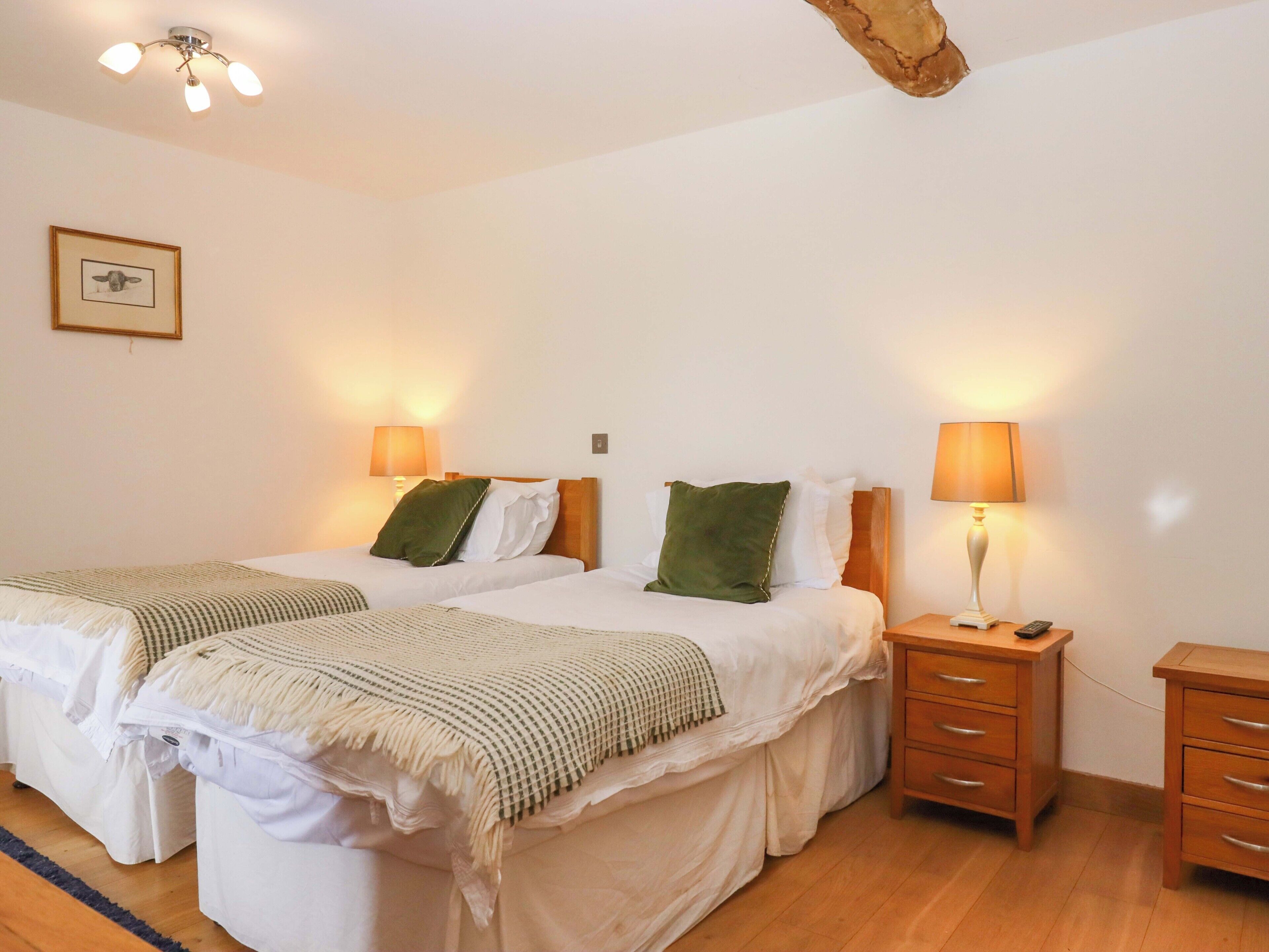 Una habitación de hotel con dos camas, lámparas de noche, una mesita de madera y una pequeña cómoda.
