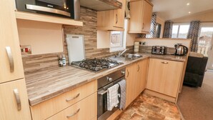A compact kitchen with a gas stove, microwave, and oven, wooden cabinets, and a tiled backsplash. - 6 Sherwood (Carnforth)