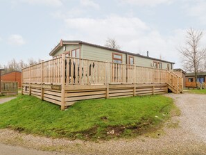 A single-story wooden house with a deck, a staircase, and a gravel driveway. - 6 Sherwood (Carnforth)