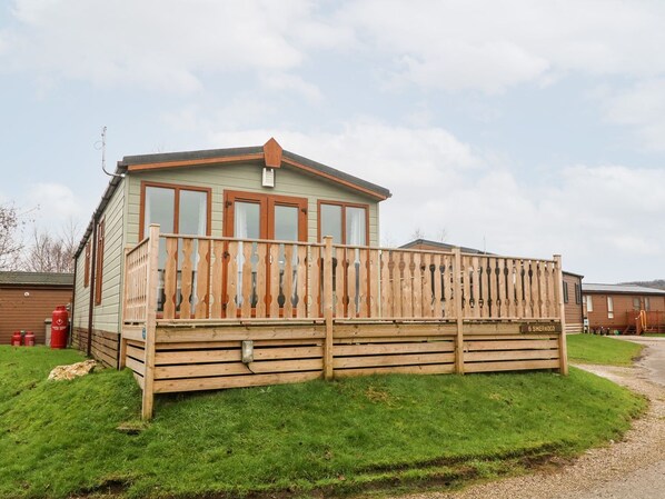 A single-story mobile home with a wooden deck and a fenced backyard. - 6 Sherwood (Carnforth)