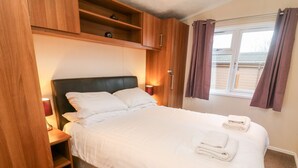 A neatly made bed with white linens, a wooden headboard, and a bedside table with a lamp. - 6 Sherwood (Carnforth)