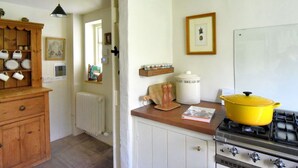 Una cocina con un armario de madera, un radiador blanco, una olla amarilla en la estufa y un cuadro en la pared.