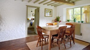 Un comedor con mesa y sillas de madera, una ventana con cortinas y vista a una cocina.