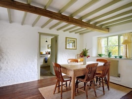 Un comedor con mesa y sillas de madera, una ventana con cortinas y vista a una cocina.