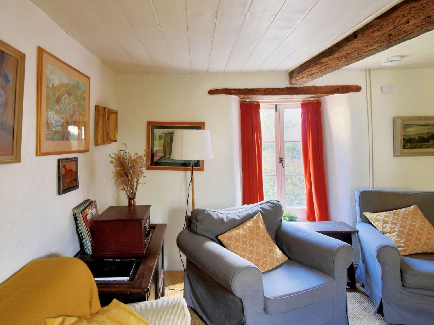 A cozy living room with a sofa, armchairs, a lamp, and framed artwork on the walls.