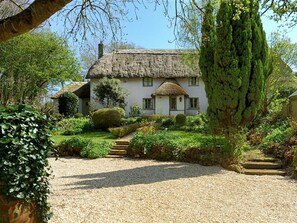 A traditional thatched-roof house with a gravel driveway and a well-maintained garden.
