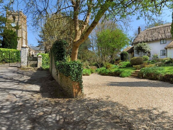 A historic stone gate, a large tree, a thatched-roof house, and a church tower.