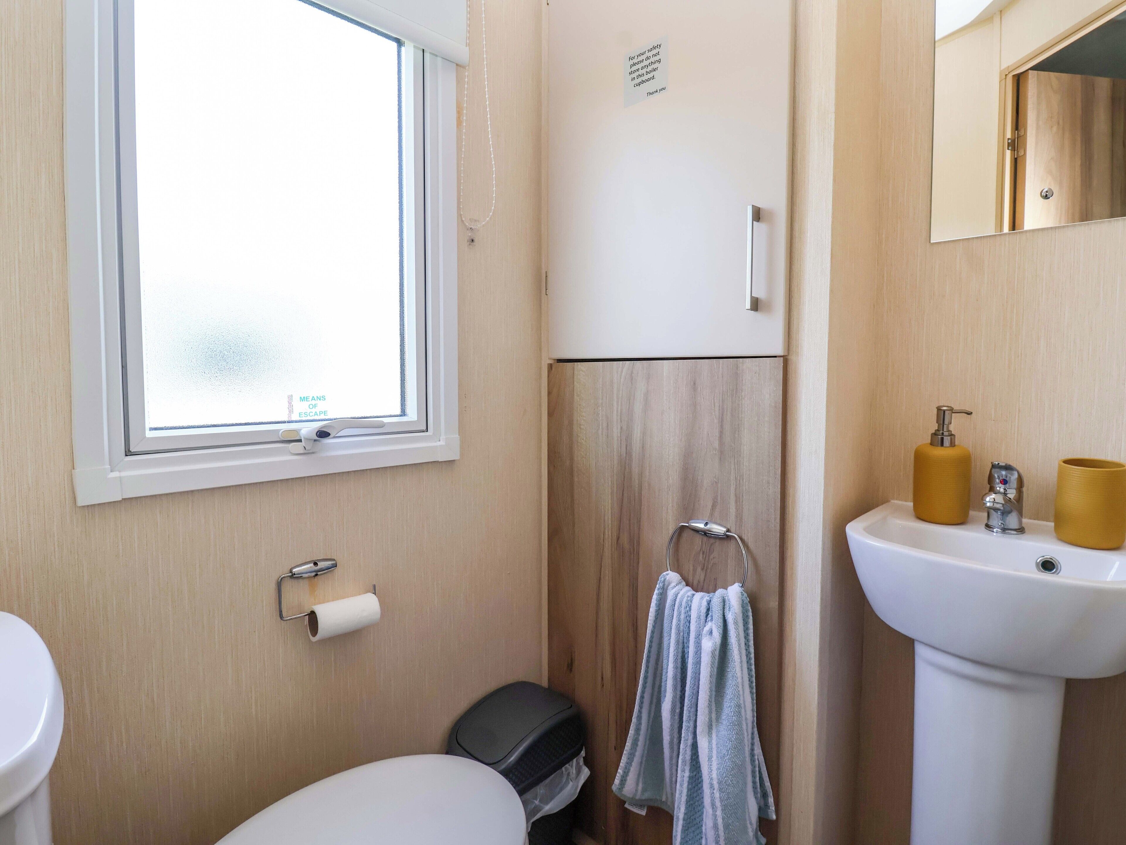 Un baño pequeño con ventana, inodoro, lavamanos y barra para toallas.
