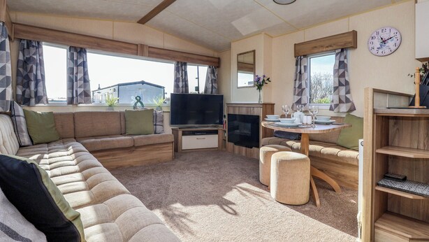 Interior acogedor de una caravana con sofá, televisión, mesa de comedor y un reloj en la pared.