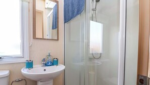 Un baño con ducha de vidrio, lavamanos sobre pedestal y espejo sobre el lavamanos.