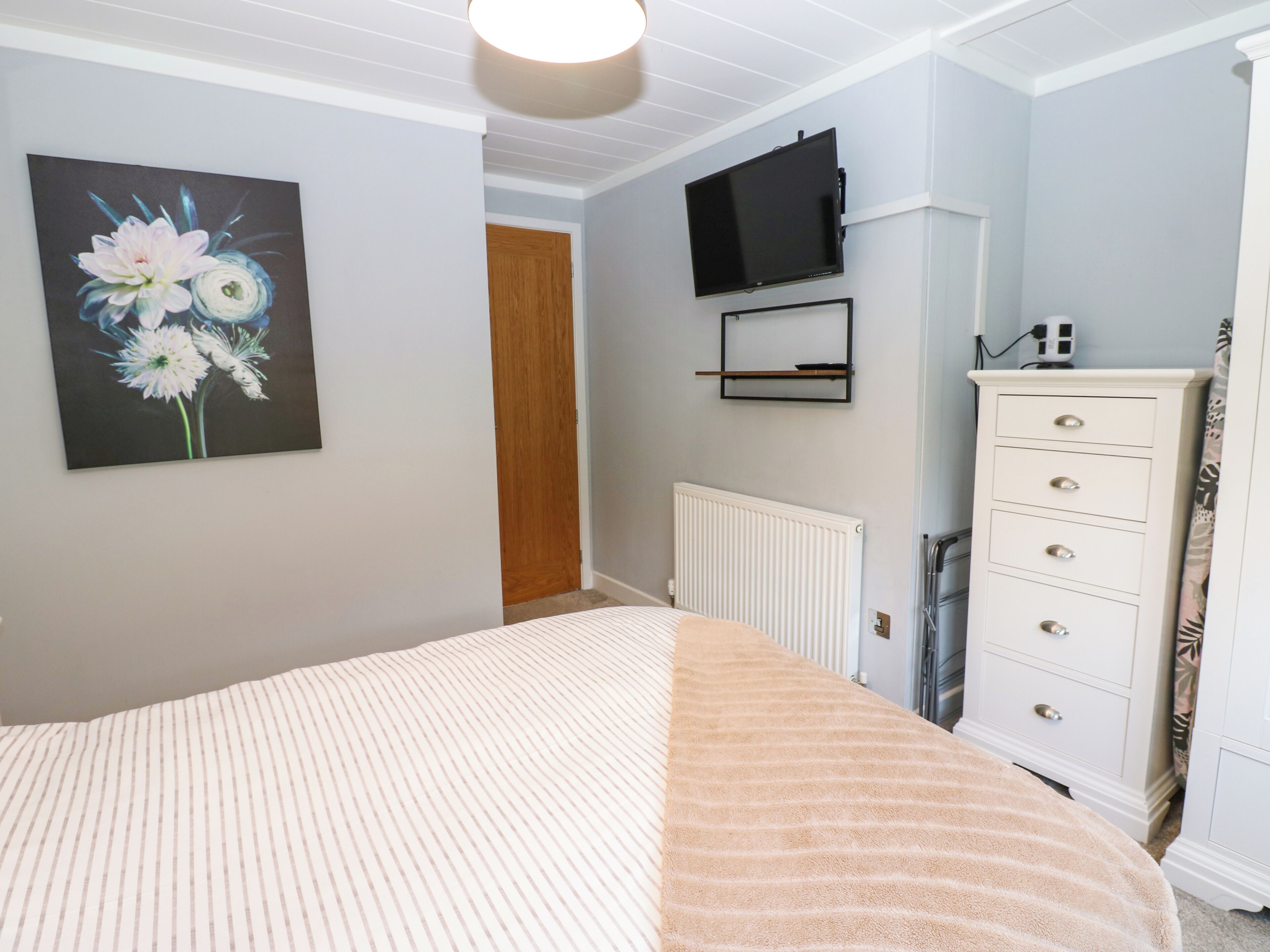 A bedroom with a bed, a dresser, a television mounted on the wall, and a painting of flowers.