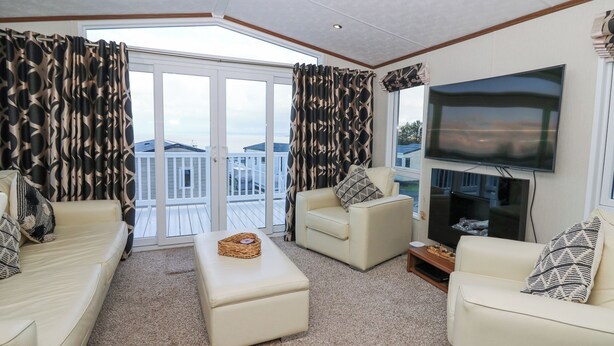 A spacious living room with a large TV, comfortable seating, and a balcony with a view. - Ocean View (New Quay)
