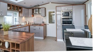A modern kitchen with a skylight, built-in appliances, and a wooden island. - Ocean View (New Quay)