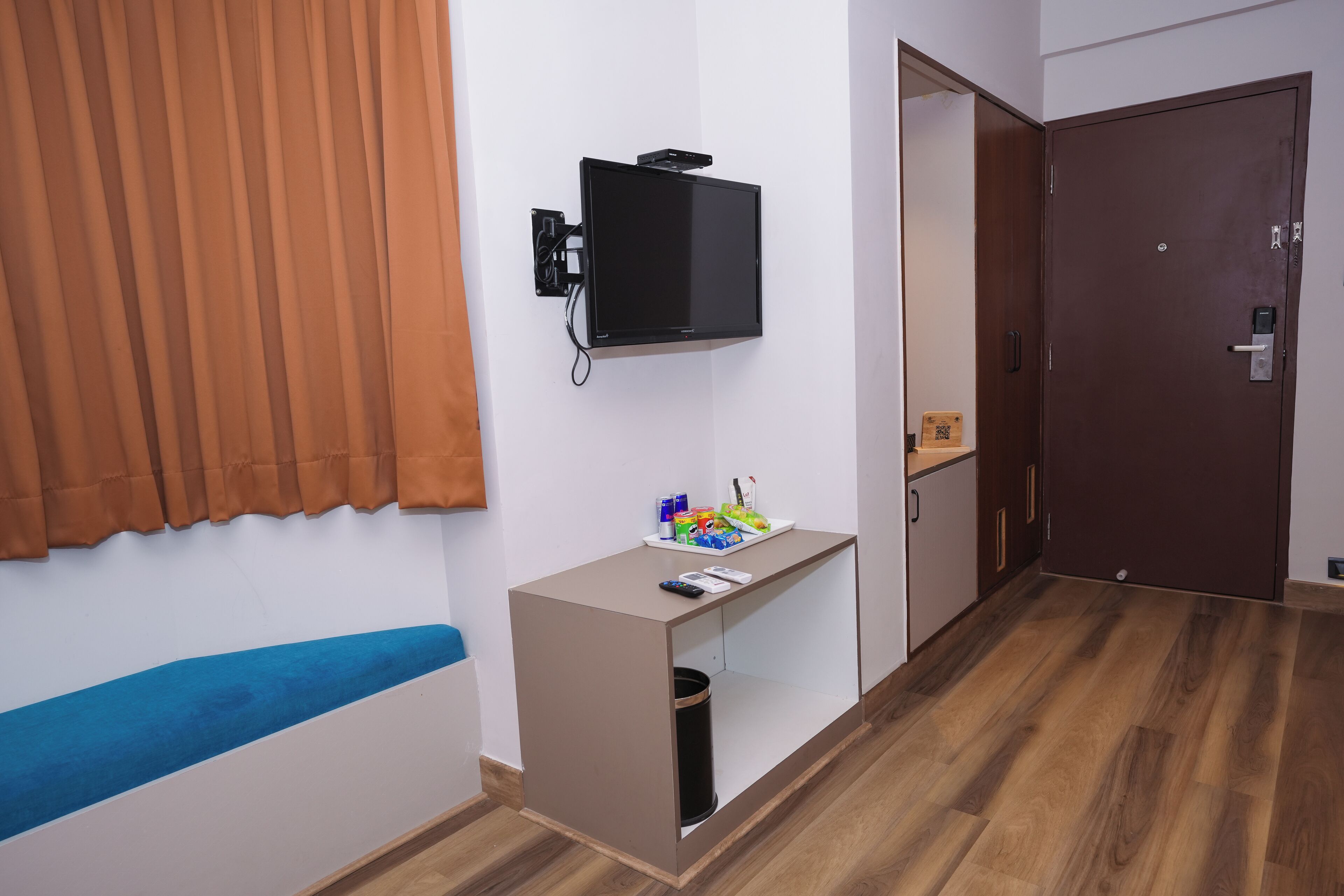 A room with a bed, a desk with a television, a trash can, and a door.