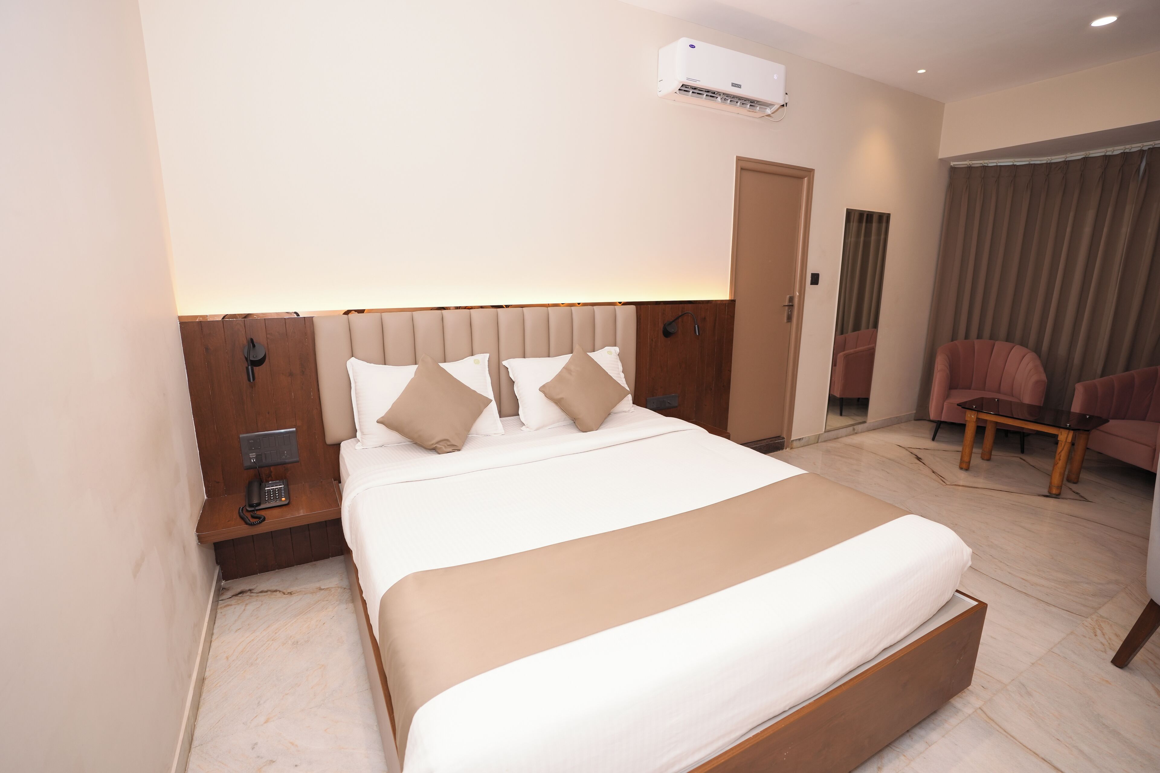 Une chambre d’hôtel avec un grand lit, une table de chevet avec un téléphone, un climatiseur fixé au mur et un coin salon comprenant une chaise et une table.