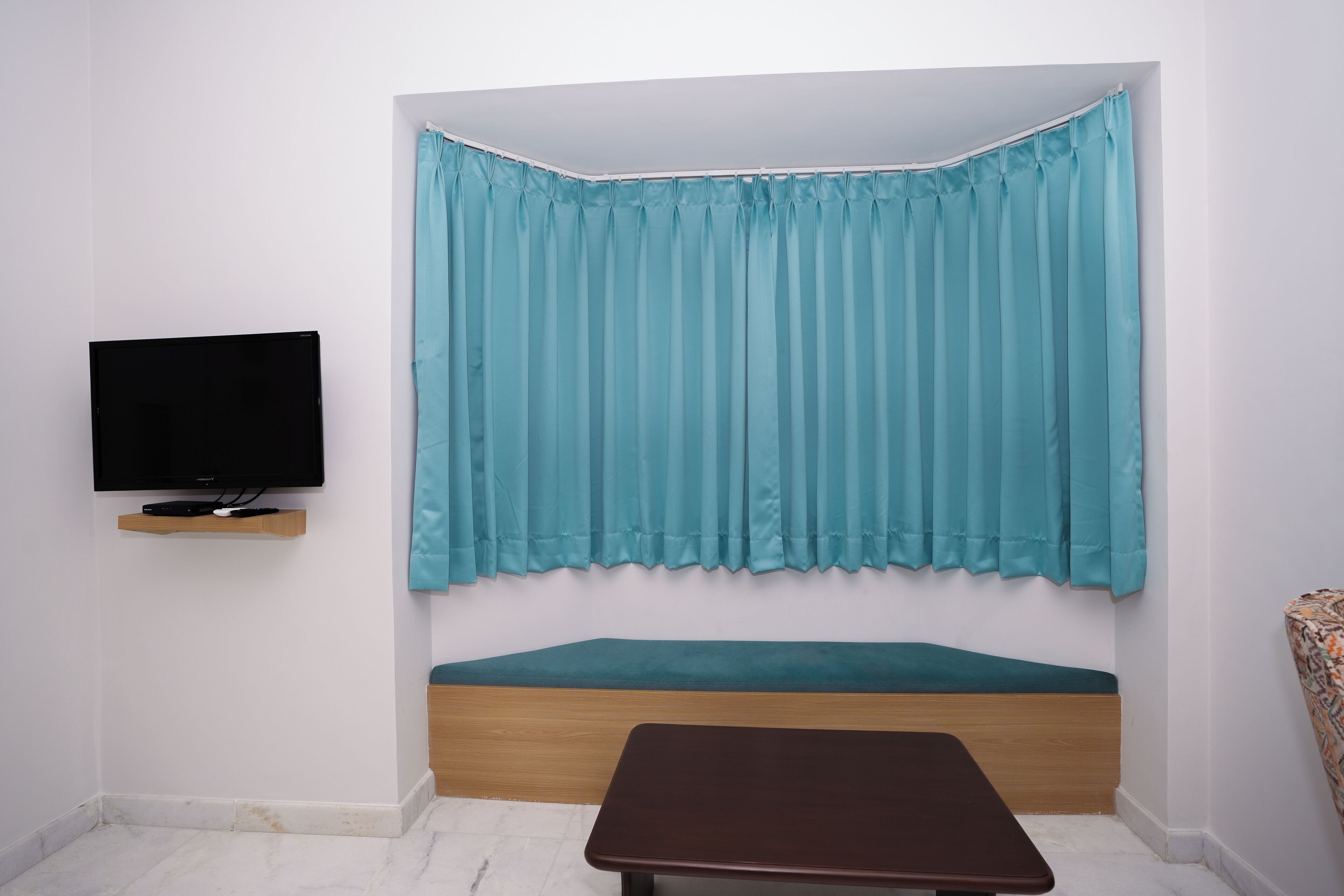 Ein Zimmer mit einem Bett, einem an der Wand befestigten Fernseher und einem Fenster mit Vorhang.