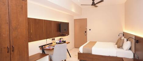 A modern hotel room with a wooden desk, a bed, a ceiling fan, and a TV mounted on the wall.