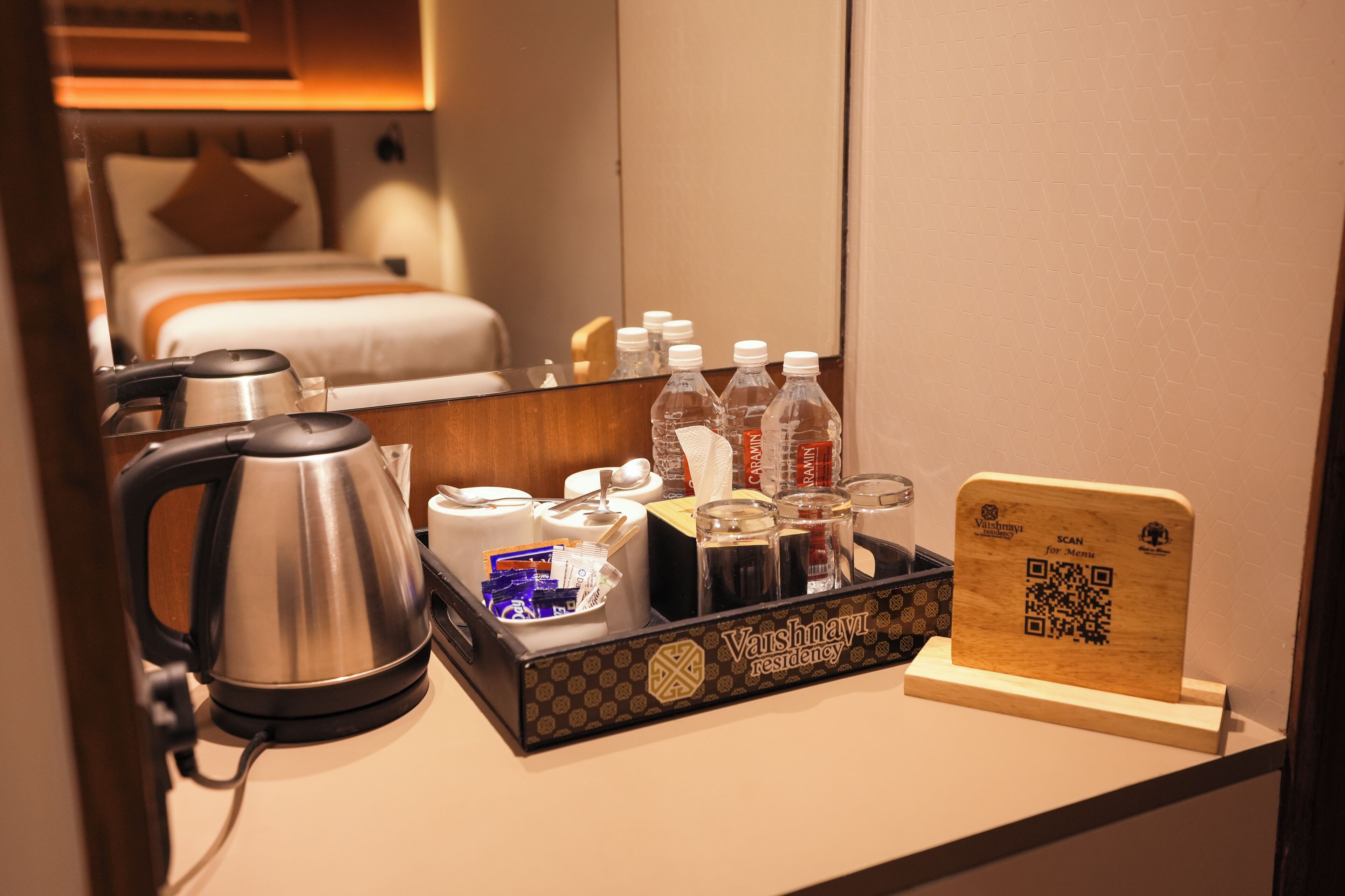 A hotel room with a bed, a kettle, a tray with toiletries, and a QR code for room service.
