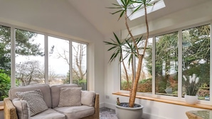 A cozy room with a wicker sofa, a large potted plant, and patterned floor tiles. - The Pines (Skipton)