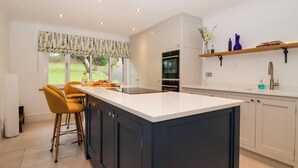 A modern kitchen with a large island, bar stools, an oven, and a window with a view of the outdoors. - The Pines (Skipton)