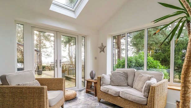 A sunlit room with wicker furniture, large windows, and a tiled floor. - The Pines (Skipton)