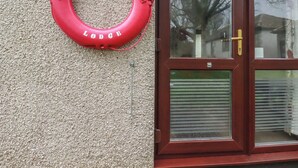 Ein roter Rettungsring mit dem Schriftzug "Saltwater Lodge", befestigt an einer strukturierten Wand neben einer Holztür mit einer Glasscheibe.