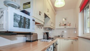 Eine Küche mit weißen Schränken, einer Holz Arbeitsplatte, einer Mikrowelle, einem Toaster, einem Spülbecken und einem Fenster mit Blick auf Bäume.