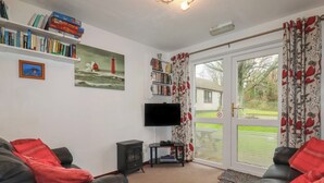 Ein Wohnzimmer mit Kamin, Flachbildfernseher, Bücherregal und einem großen Fenster mit Vorhängen.