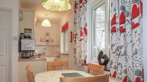 Eine kompakte Küche mit Kühlschrank, Mikrowelle und Spüle. Ein Esstisch mit Stühlen und ein Fenster mit blumigen Vorhängen.