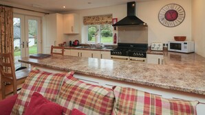 Een moderne keuken met een centraal eiland, een ingebouwde oven, magnetron en een grote wandklok.