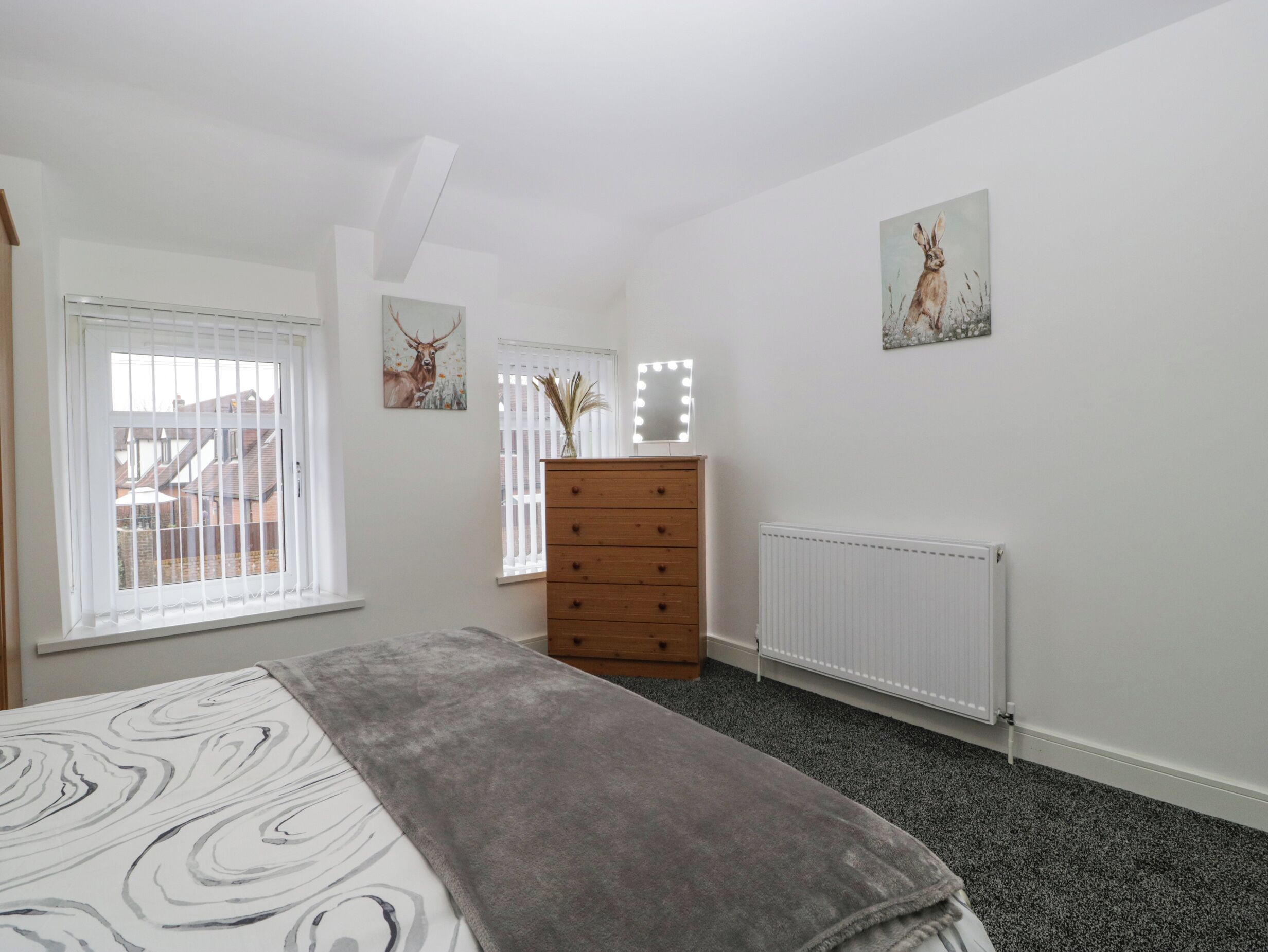 A bedroom with a bed, dresser, two windows, and a radiator.