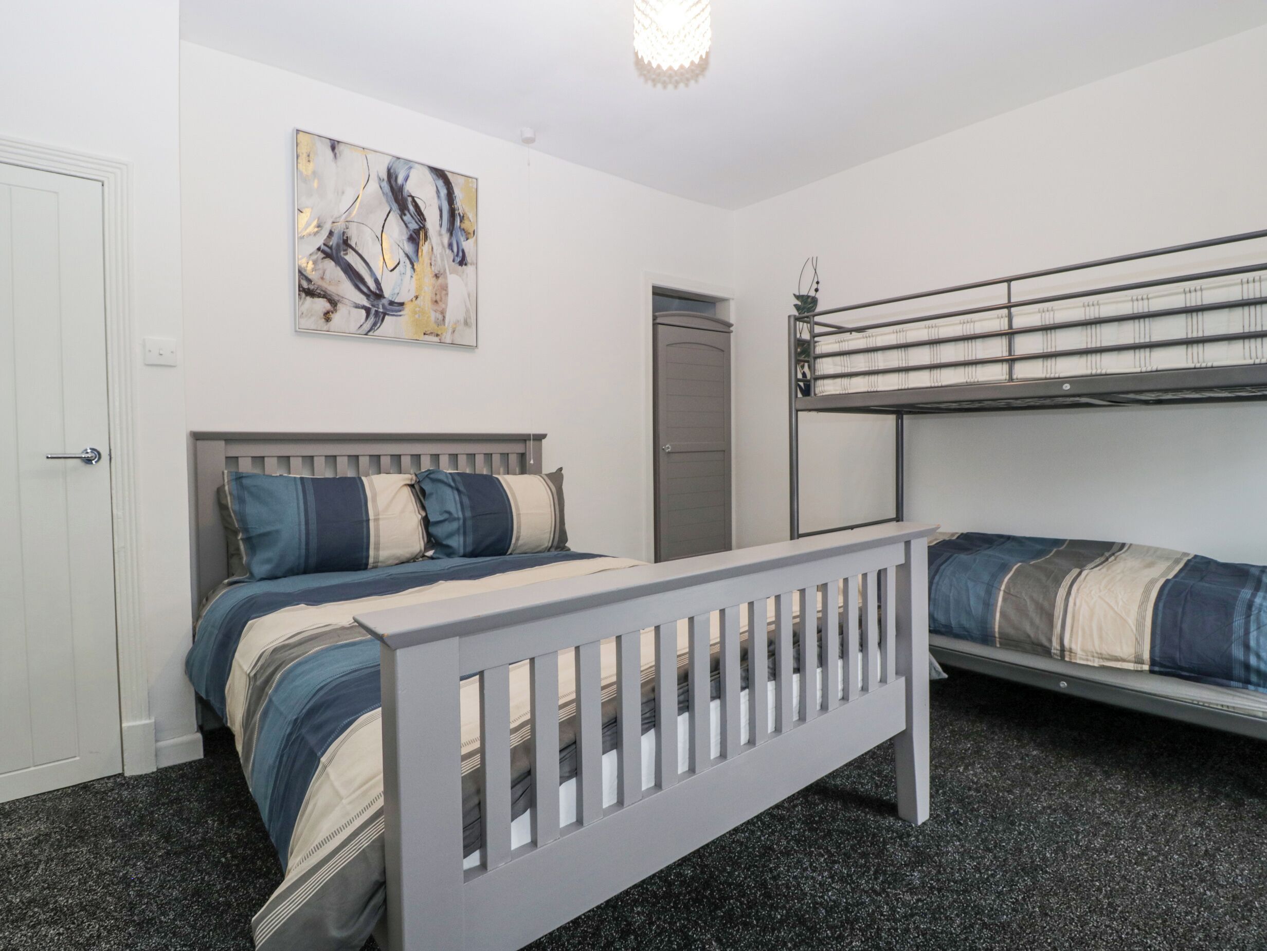 A bedroom with a bunk bed, a single bed, a door, and a painting on the wall.