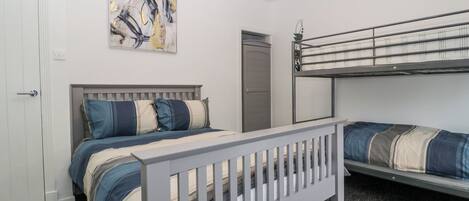 A bedroom with a bunk bed, a single bed, a door, and a painting on the wall.