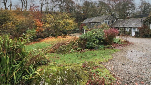 A stone house with a gravel driveway and a garden with autumn foliage.