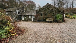 A stone cottage with a gravel driveway and a bench.